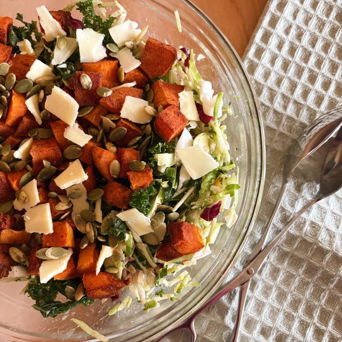 kale butternut squash salad in bowl with tongs and blue towel
