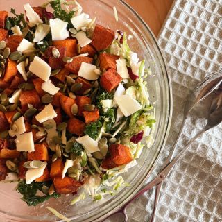 kale butternut squash salad in bowl with tongs and blue towel