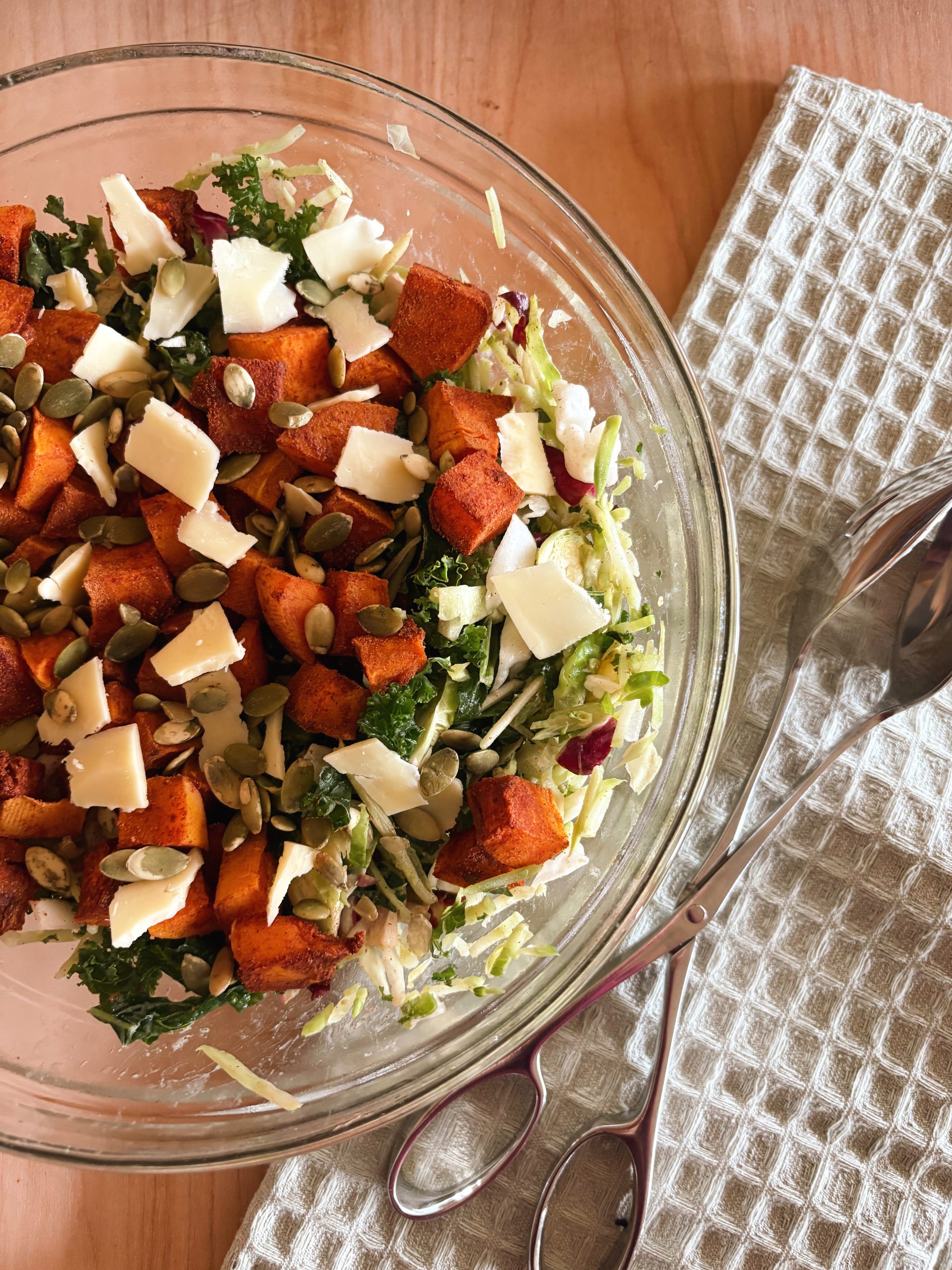 kale butternut squash salad in bowl with tongs and blue towel
