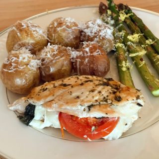 caprese stuffed chicken on plate with potatoes and asparagus